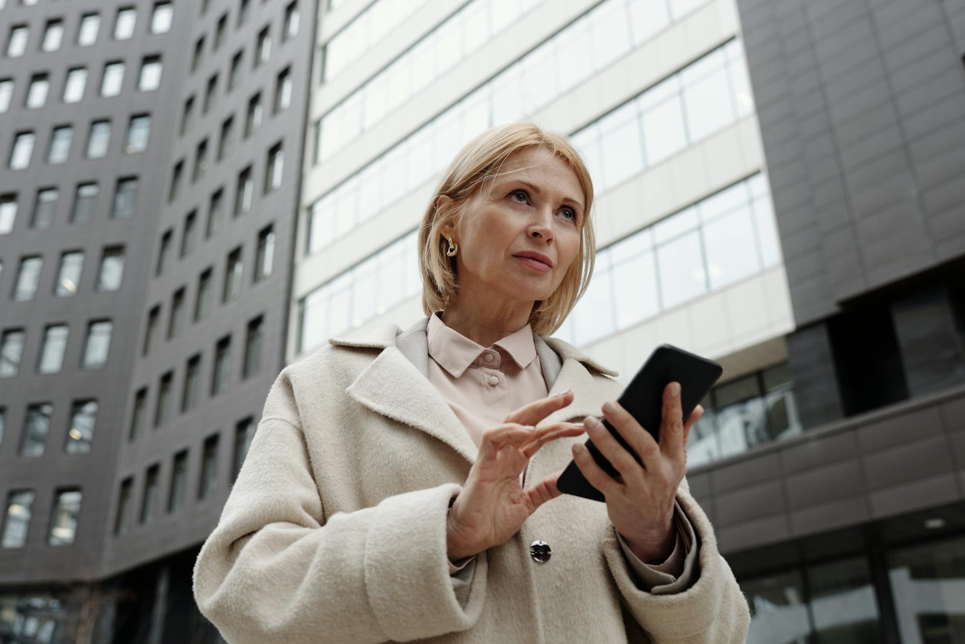 woman in beige coat holding a cellphone