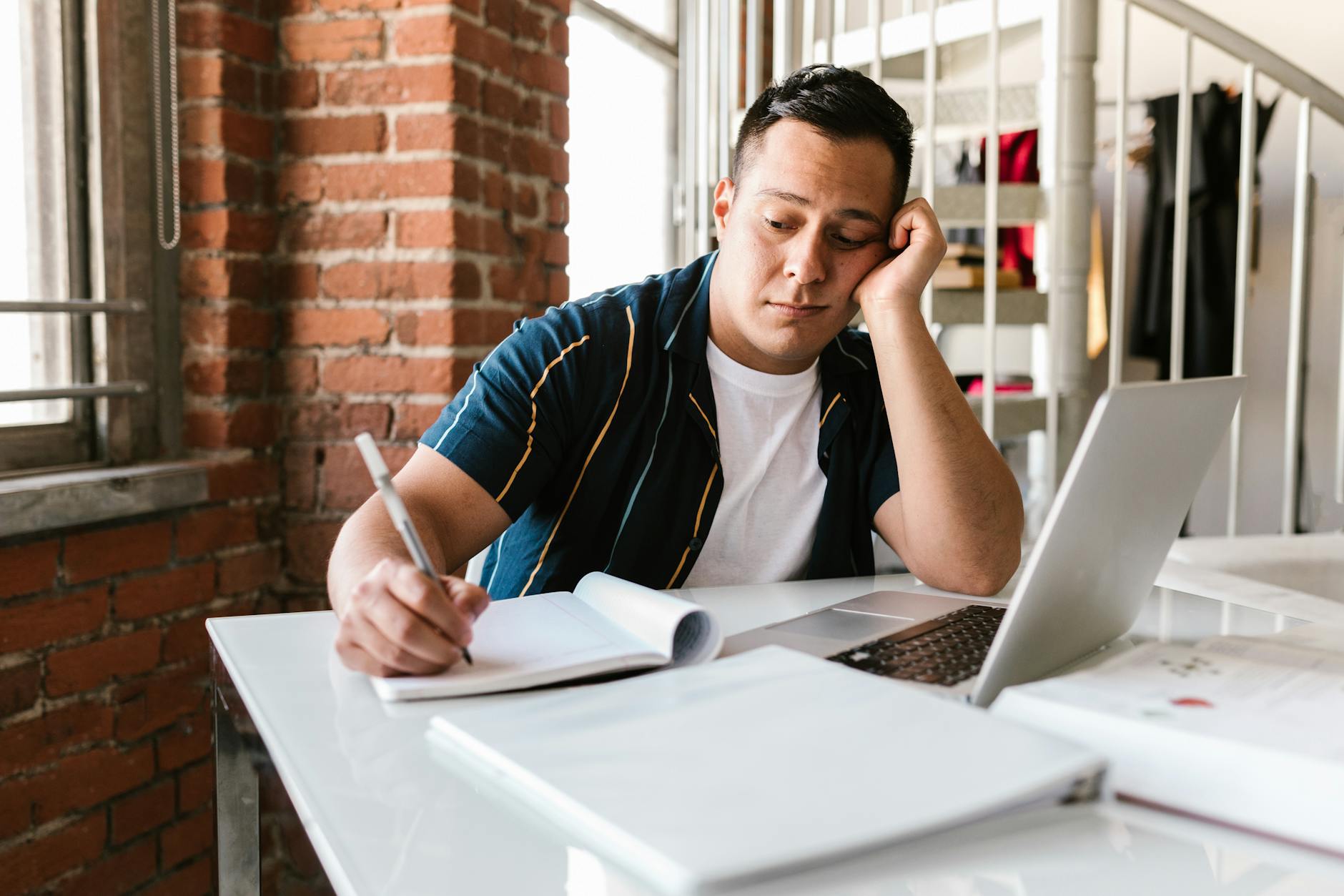 a bored man writing on a notebook